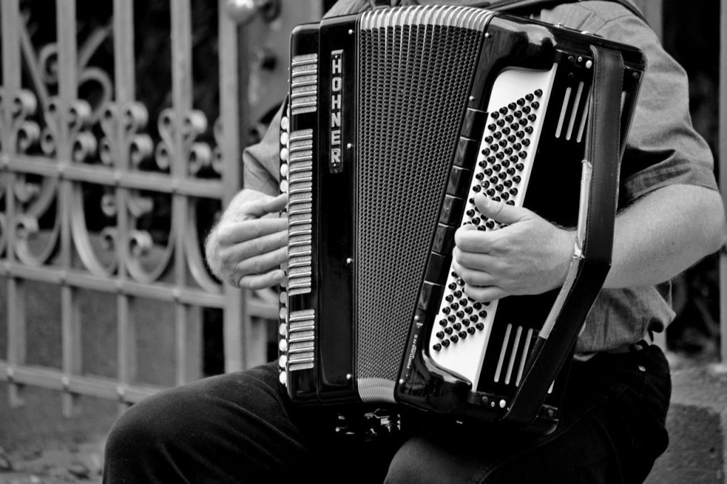 A black and white photo of a street musician playing an accordion, showcasing the instrument and musicians hands.
